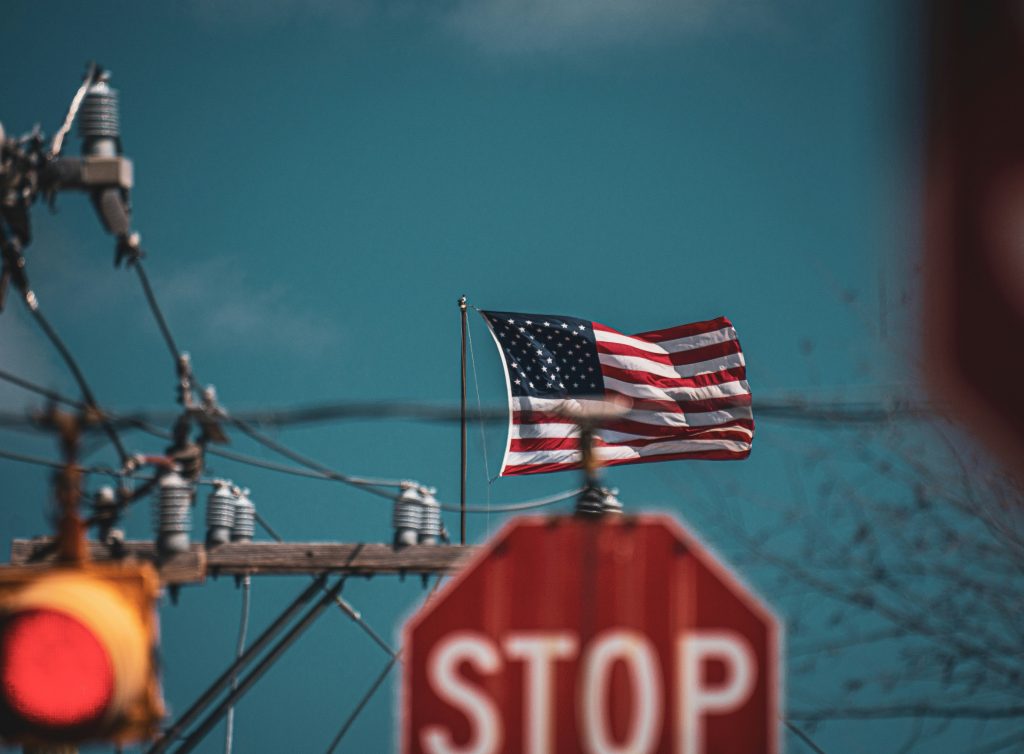 USA flag and stop sign with power lines in background, symbolizing trade restrictions and supply chain impact